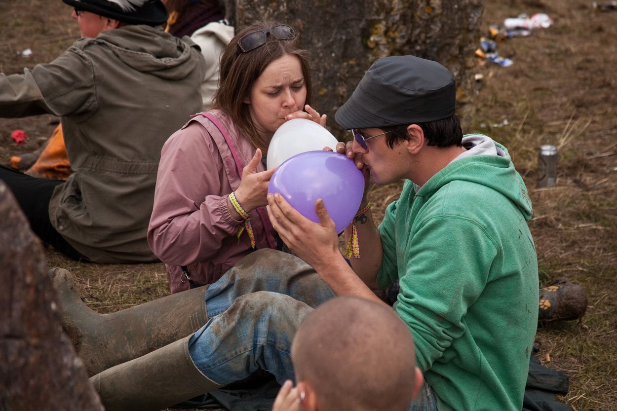 Couple breathing in balloons of nitrous oxide - laughing gas at the stone circle in Kings Meadow, Glastonbury Festival 2011